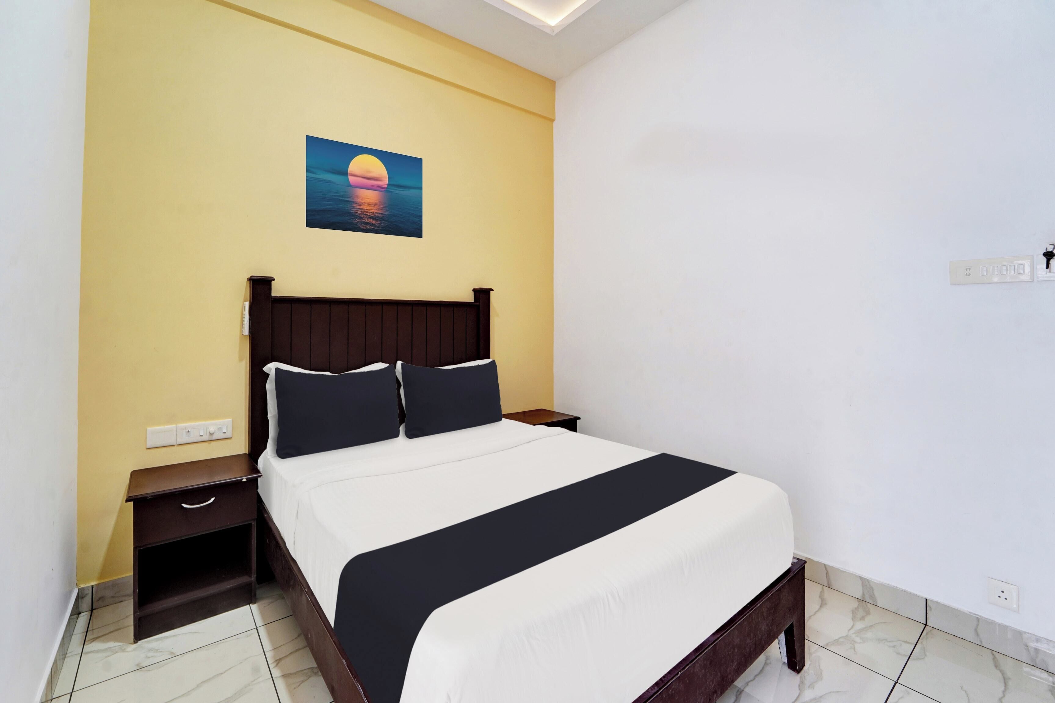 Habitación de hotel con cama, mesita de noche, un cuadro en la pared y un enchufe.