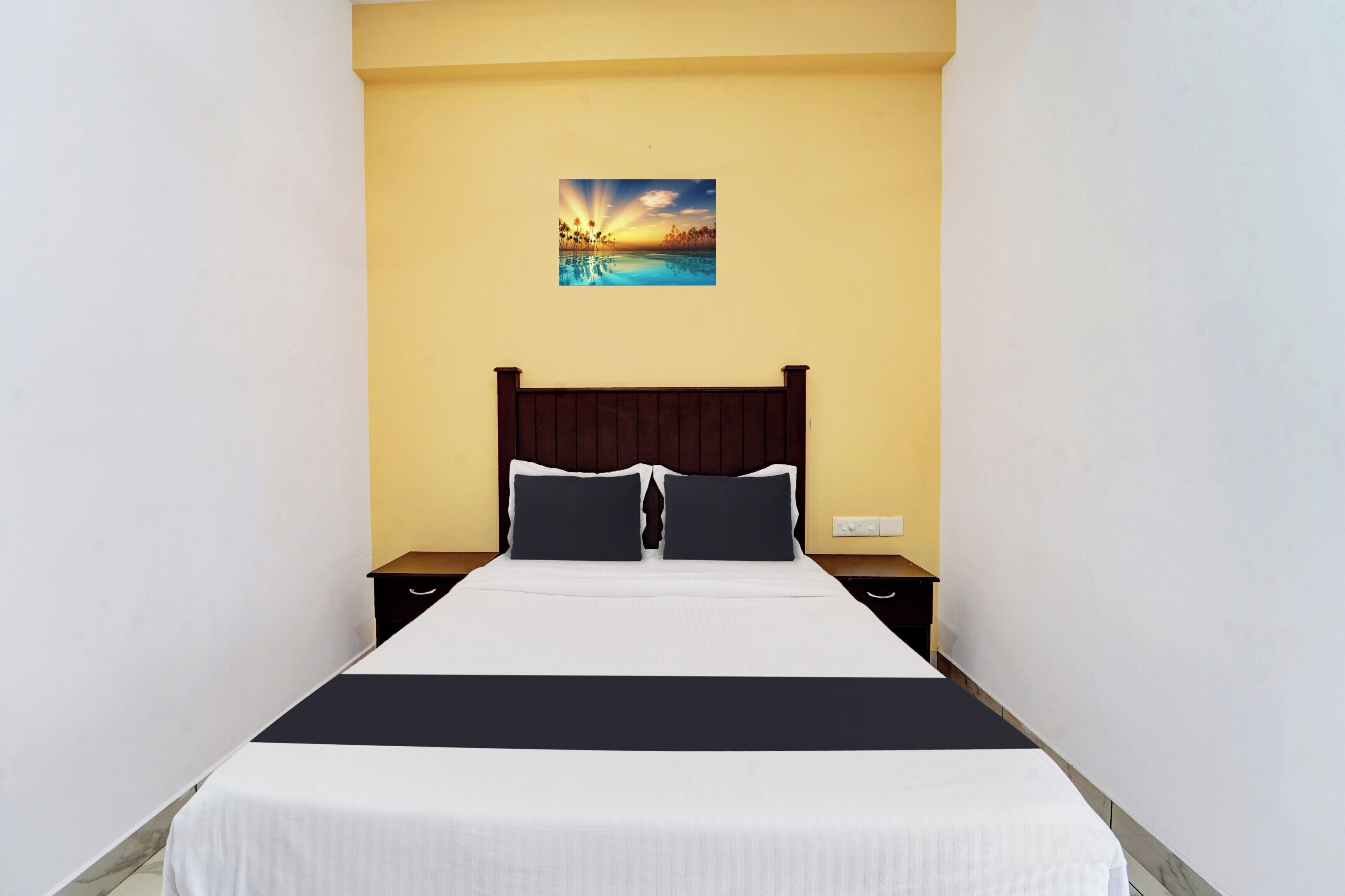 A hotel room with a bed, two bedside tables, a nightstand, and a painting on the wall.