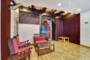 Una habitación con suelo de madera, una cortina roja, una mesa de vidrio y dos sillas rojas.