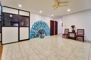 A hallway with a peacock mural, a ceiling fan, and a seating area with chairs and a table. - Collection O Calvathy Road Near Fort (Kochi)