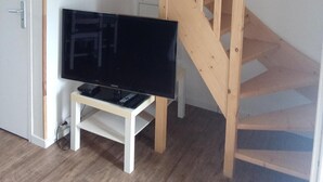 Een houten trap die naar een verdieping leidt, een witte deur en een televisie op een witte standaard.