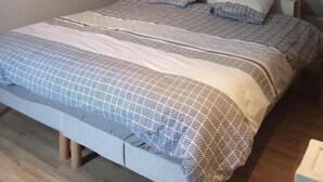 Een eenpersoonskamer met een schuine kap, een bed met een patroon eroverheen en een nachtkastje.