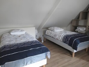Une chambre à coucher avec deux lits, chacun agrémenté de draps et d’oreillers à motifs, une table de chevet avec une lampe et une étagère en bois où sont pliés des vêtements.