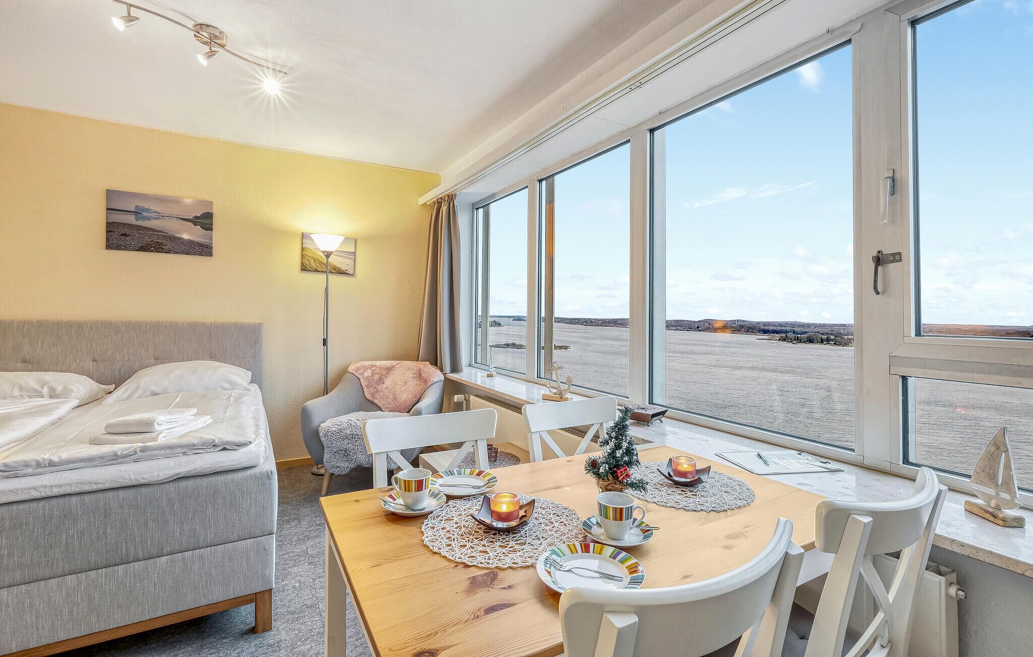 A hotel room with a bed, a table set for two with a candle, and a view of a river.