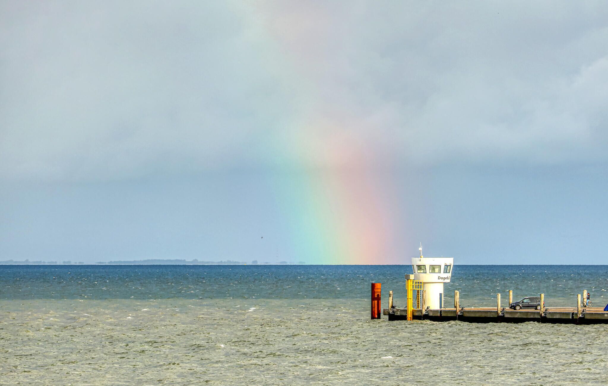 A coastal scene with a lighthouse, a pier, and a rainbow.
