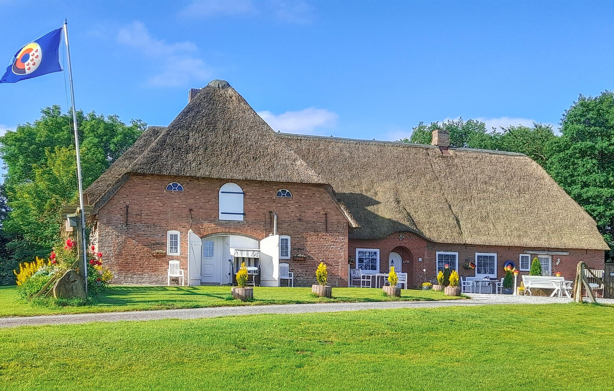 A traditional brick building with a thatched roof, a flagpole with a flag, and a well-maintained lawn.