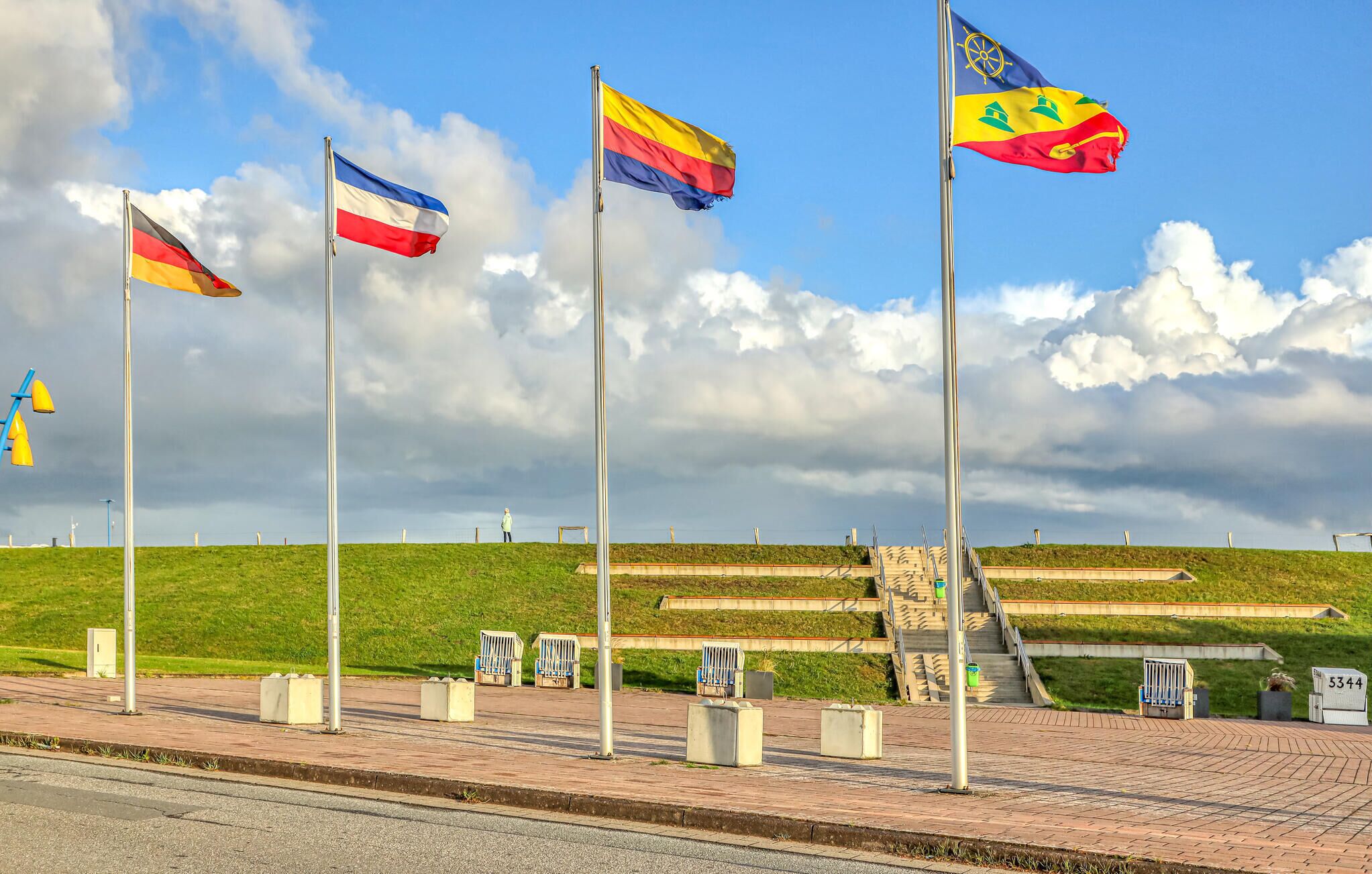 A series of flags on flagpoles, a grassy hill, and a paved area with benches.