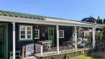 Une maison traditionnelle en bois, avec une porte verte, des fenêtres à cadre blanc et une véranda couverte aménagée avec du mobilier d’extérieur.