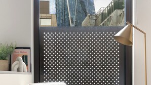 A modern chair with a textured cushion and a single decorative pillow, positioned in front of a window with a view of a cityscape. - Jitaku by Residence Apartments (London)