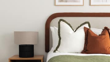 A neatly arranged bedroom with a bed, pillows, a bedside table with a lamp, and framed artwork on the wall.