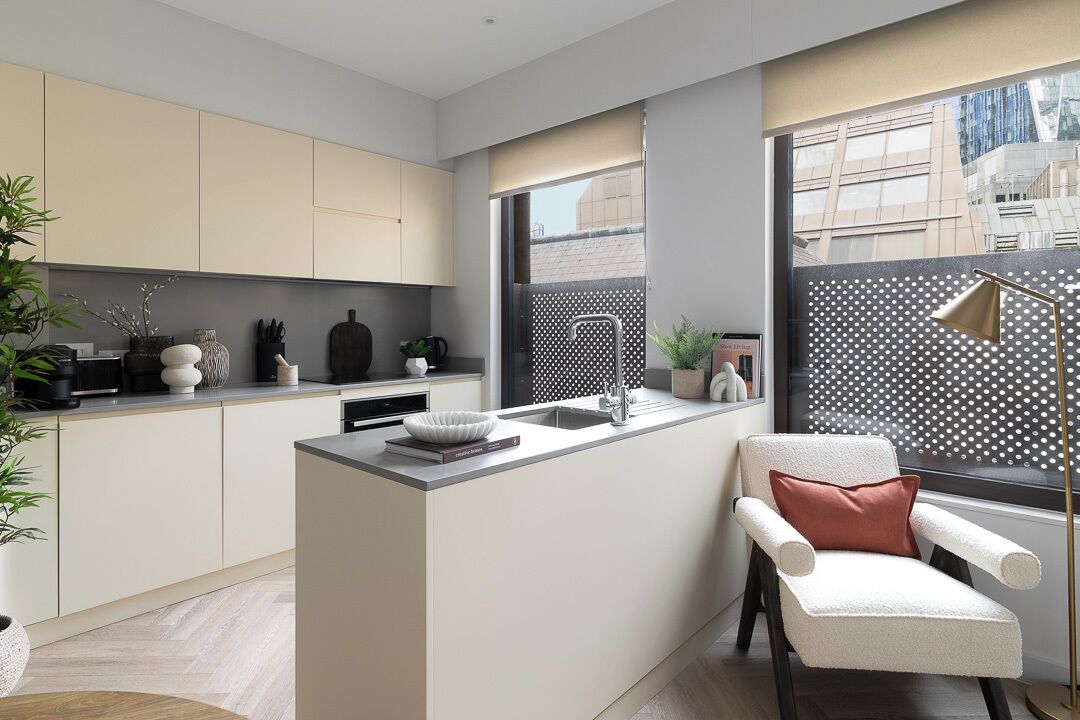 Una cocina moderna con una isla central, un comedor con una silla y un ventanal con vistas a edificios.