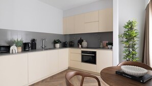 A modern kitchen with light-colored cabinets, a dark countertop, and a dining area with a wooden chair and a book titled 'Art in Residence'. - Jitaku by Residence Apartments (London)