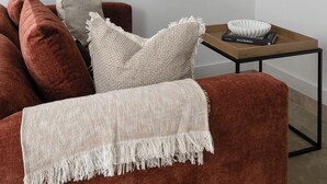 A living room with a sofa, pillows, a throw blanket, a coffee table with a book and a bowl, a wall-mounted mirror, and a flat-screen TV. - Jitaku by Residence Apartments (London)