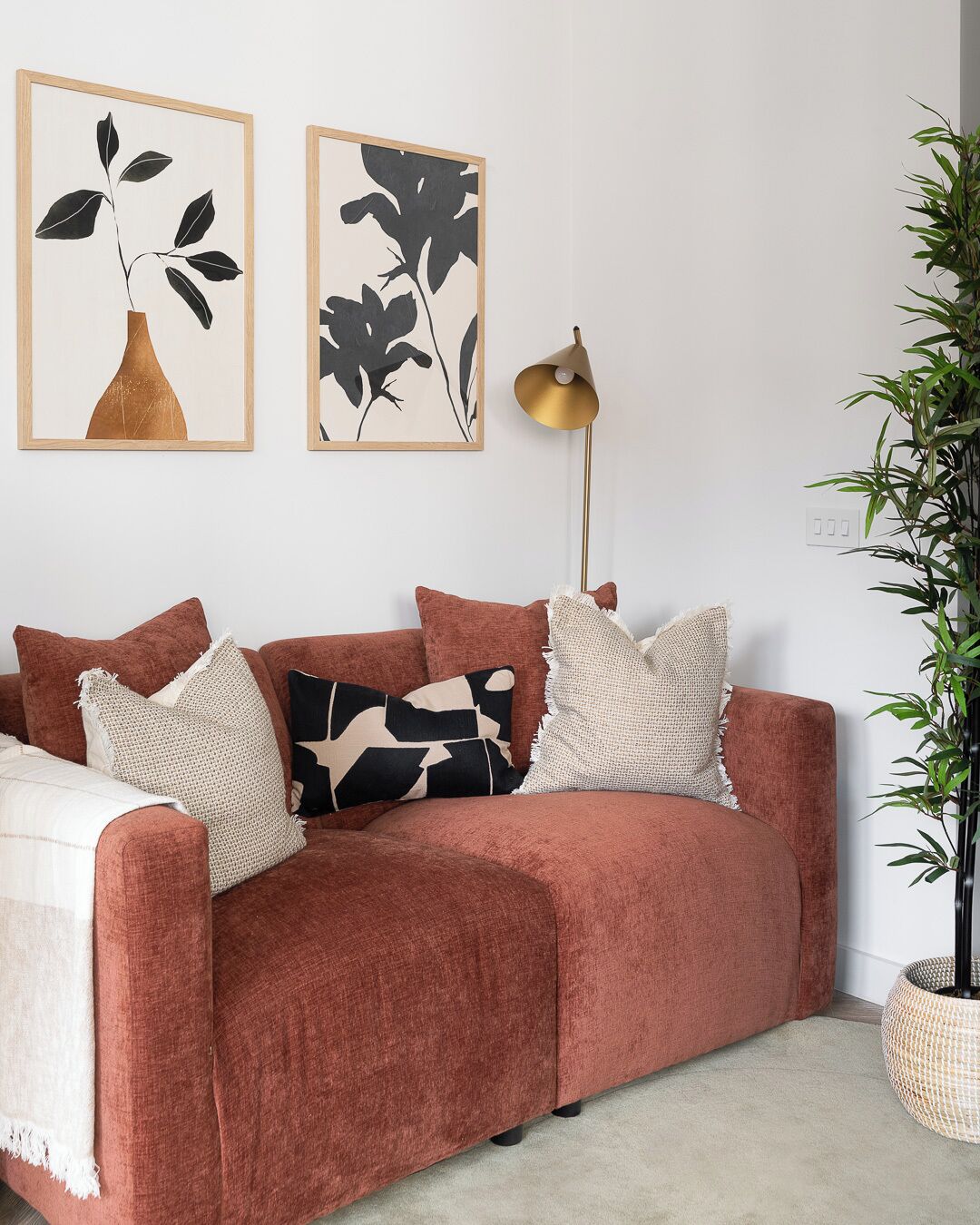 A room with a red sofa, two framed artworks, a floor lamp, and a potted plant.