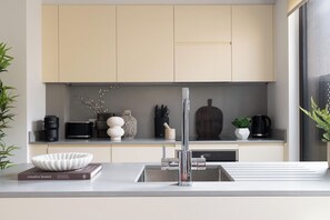 A modern kitchen with a sleek faucet, a bowl on the counter, and various kitchen items. - Jitaku by Residence Apartments (London)