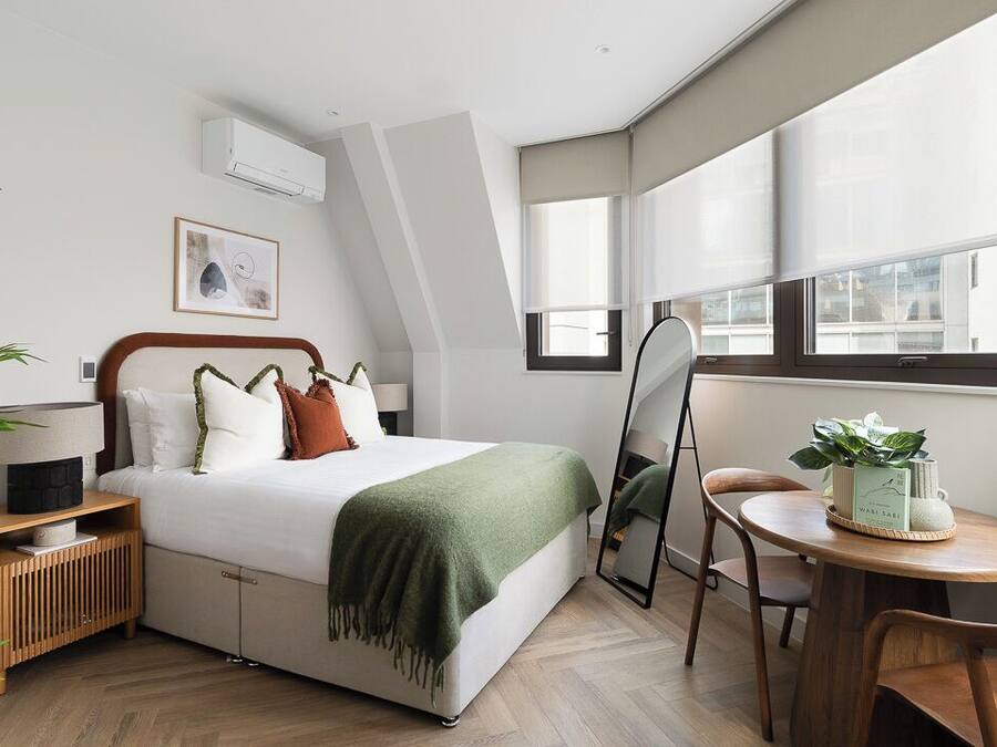 A modern bedroom with a bed, bedside table, mirror, and a small round table with a plant.