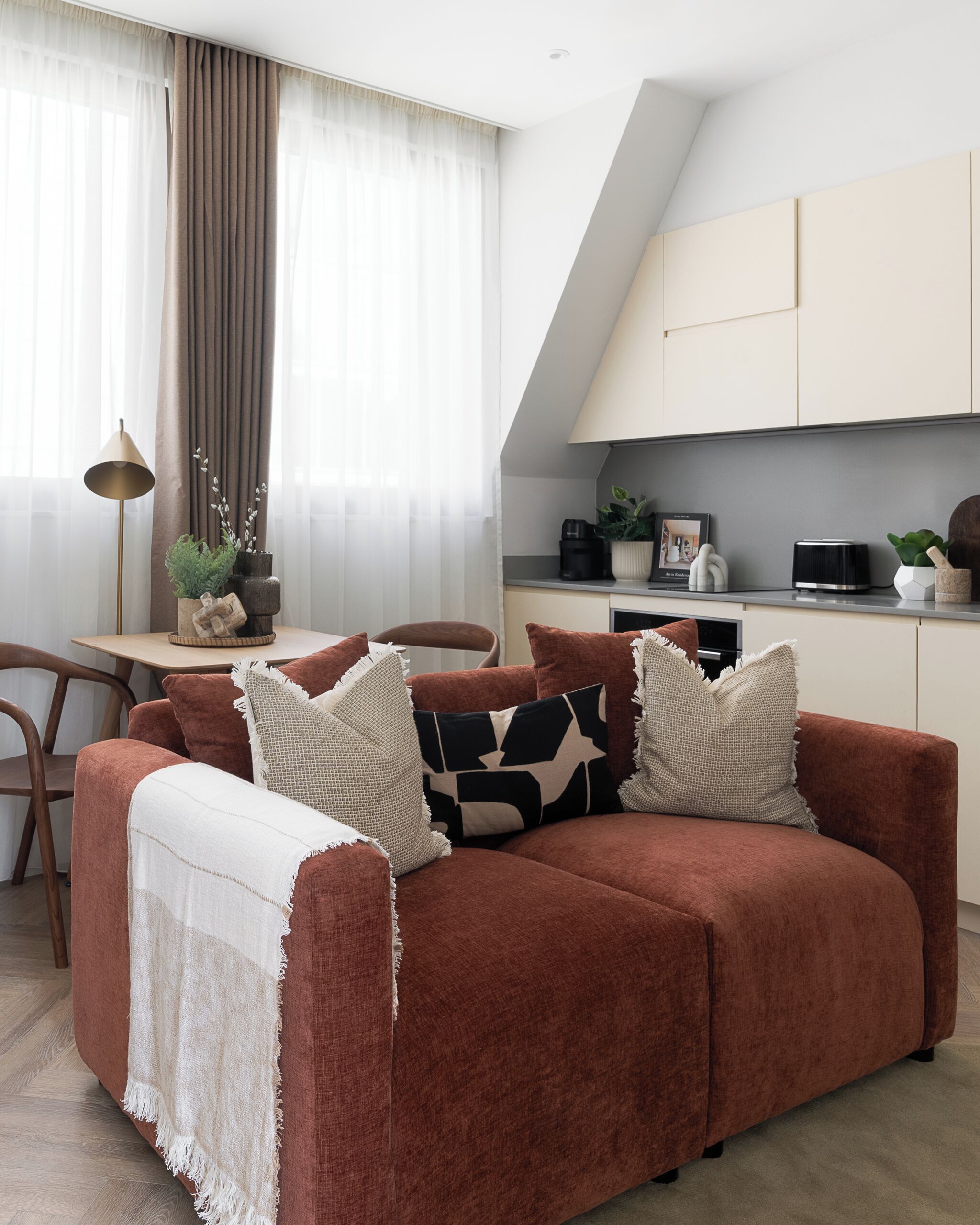 A modern living room with a brown sofa, a dining table, and a kitchen area.