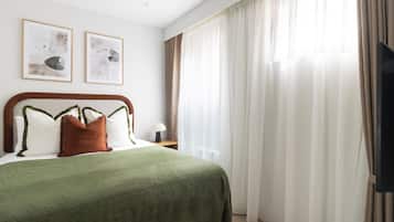 Ein Hotelzimmer mit einem Bett, einem Nachttisch, einer Lampe und zwei gerahmten Kunstwerken an der Wand.