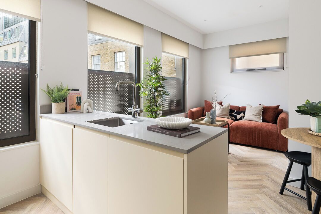 Eine moderne Küche mit einer zentralen Kochinsel, einem Essbereich mit Sofa und Tisch sowie einem großen Fenster, das für natürliches Licht sorgt.