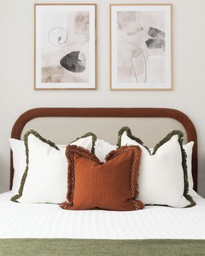 A bed with white bedding, a brown accent pillow, and green trim on the headboard. Two framed abstract artworks are hung above the bed. - Jitaku by Residence Apartments (London)