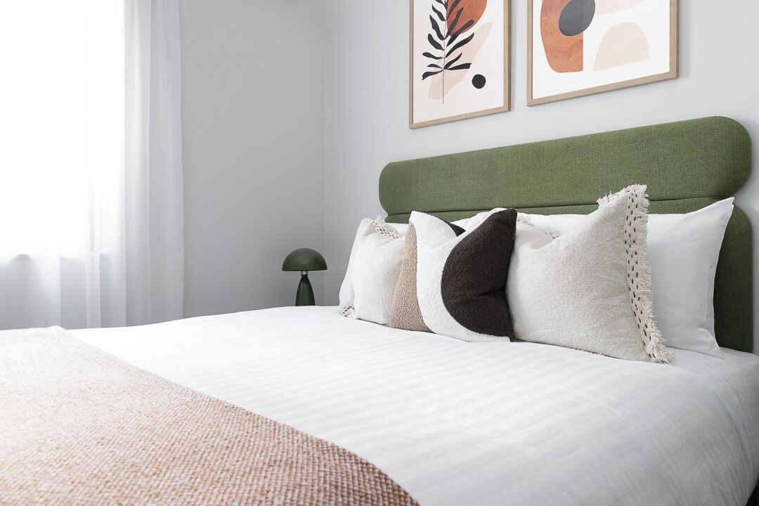 A neatly made bed with a green headboard, white bedding, and a textured throw blanket.