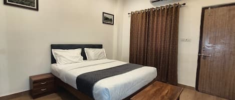 A bedroom with a bed, bedside tables, a wooden bench, a rug, a curtain, and an air conditioning unit.