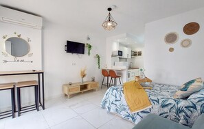 Ett modernt sovrum med en säng, ett skrivbord, en TV och en liten köksdel.