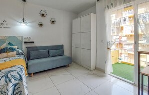 A bedroom with a bed, a blue sofa, a wardrobe, and a window with a view of a building. - Pet friendly apartment in Benalmadena with swimming pool (Benalmadena)