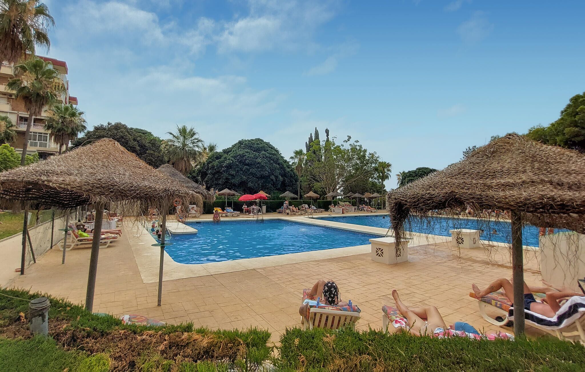 Un área de piscina con sillones de descanso y sombrillas de paja.