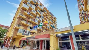 Un hotel de varios pisos con balcones, una tienda con un letrero y un cielo despejado.