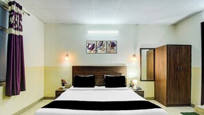 A hotel room with a large bed, a wooden wardrobe, a bedside table with a lamp, and a wall-mounted artwork. - Collection O Raja Park Jaipur (Jaipur)