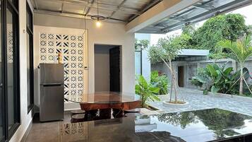 A modern kitchen with a glass-top dining table, a built-in refrigerator, and a view of a garden with a water feature.