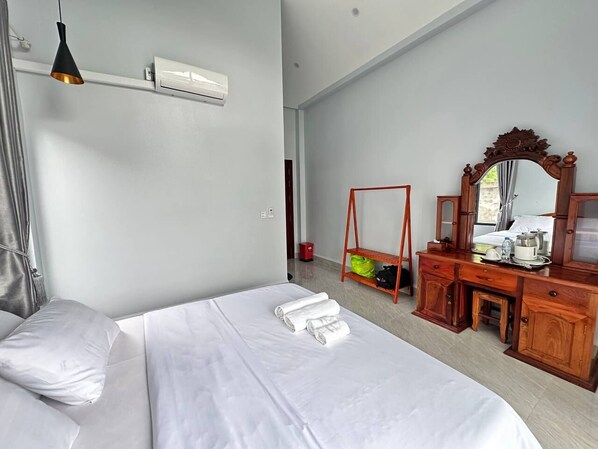 A hotel room with a bed, a wooden dresser, a mirror, and a hanging light fixture.
