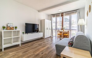 Ein modernes Wohnzimmer mit Flachbildfernseher, weißen Schränken, einem grauen Sofa und einem Essbereich mit Tisch und Stühlen.