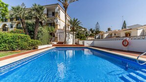 A swimming pool with clear blue water, surrounded by a white wall with a decorative pattern, and palm trees. - Gorgeous apartment in Málaga with swimming pool (Málaga)