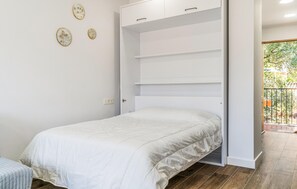 Quarto com cama, guarda-roupa e vista para um jardim através de uma porta aberta.