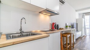 A modern kitchen with white cabinetry, stainless steel appliances, and wooden bar stools. - Gorgeous apartment in Málaga with swimming pool (Málaga)