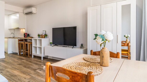 A modern living space with a flat-screen TV, wooden dining table, woven placemats, and a vase with flowers. - Gorgeous apartment in Málaga with swimming pool (Málaga)