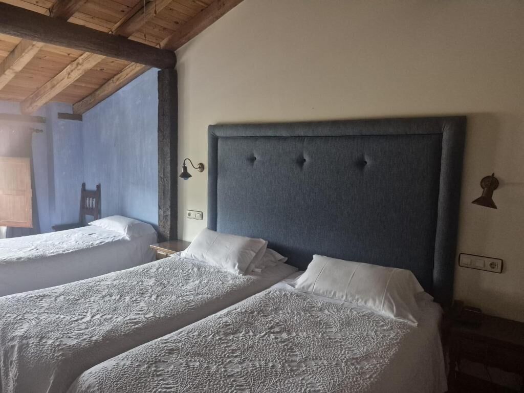 A room with two beds, a wooden ceiling, and a wall-mounted light fixture.
