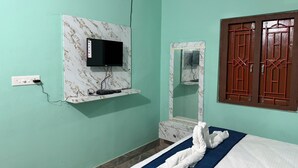 Una habitación con cama, televisión montada en una pared de mármol, espejo y armario con puerta roja.