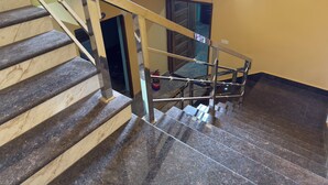 Una escalera con barandilla metálica y piso de madera, que conduce a un rellano con una puerta y un extintor.