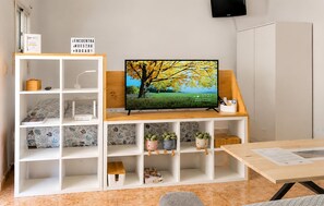 Een kamer met een televisie op een houten standaard, witte planken met diverse spullen, en een bord boven de televisie.
