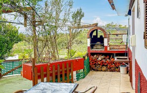 Ein Patio im Freien mit einem Grill, einem Holztisch und einem roten Zaun.