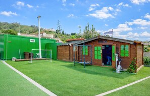 A small wooden building with a green door, a soccer goal, and a green container in a grassy area. - Los Viejitos en Firgas (Firgas)