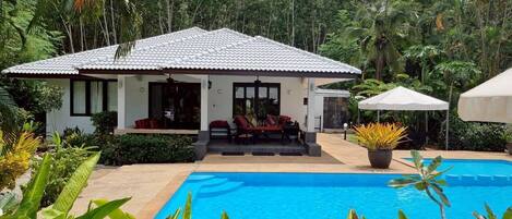A house with a pool, surrounded by lush greenery.