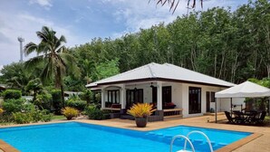 A swimming pool with a white-roofed building in the background, surrounded by lush greenery. - Baan Lompai Villa (Ao Nang)