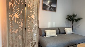 A room with a grey sofa, decorative wooden panel, a framed picture on the wall, and a small tree plant. - 4★ Cozy Apartment in Contrexéville Thermal Baths (Contrexéville)