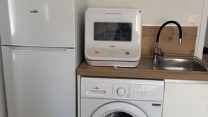 A compact kitchen with a refrigerator, a coffee maker, and a washing machine. - 4★ Cozy Apartment in Contrexéville Thermal Baths (Contrexéville)
