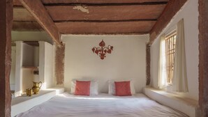 Una camera da letto con un letto, due cuscini, un elemento decorativo a parete, una finestra con grate e una mensola con oggetti.