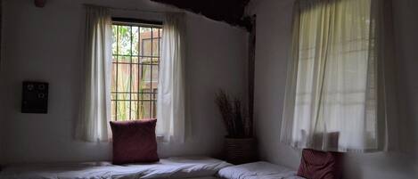 A room with two beds, a window with bars, and a wall-mounted switch.